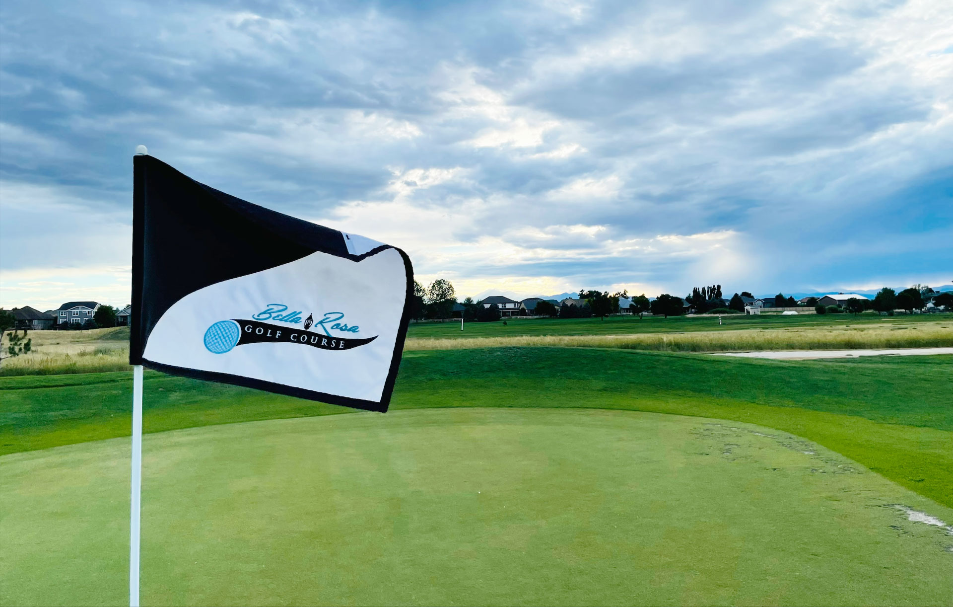 Flag of Bella Rose Golf Course on a green with a cloudy sky in the background.
