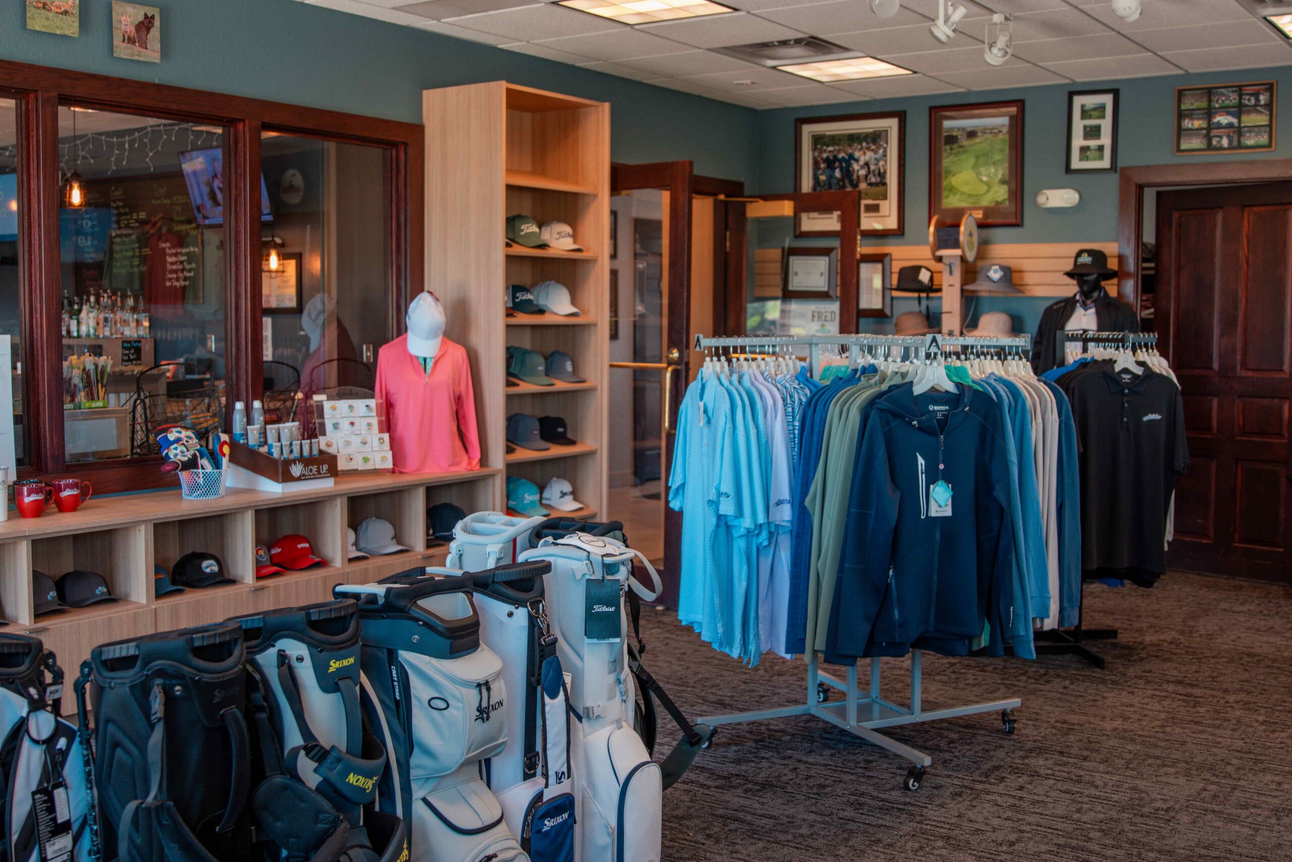 Interior of a golf shop featuring clothing racks, golf bags, and a display counter with merchandise.