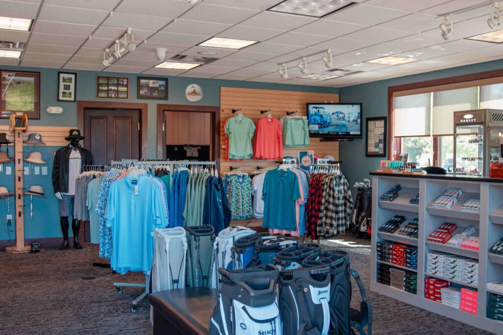 Interior of a golf shop showcasing clothing, golf bags, and accessories with a TV displaying a golf scene.