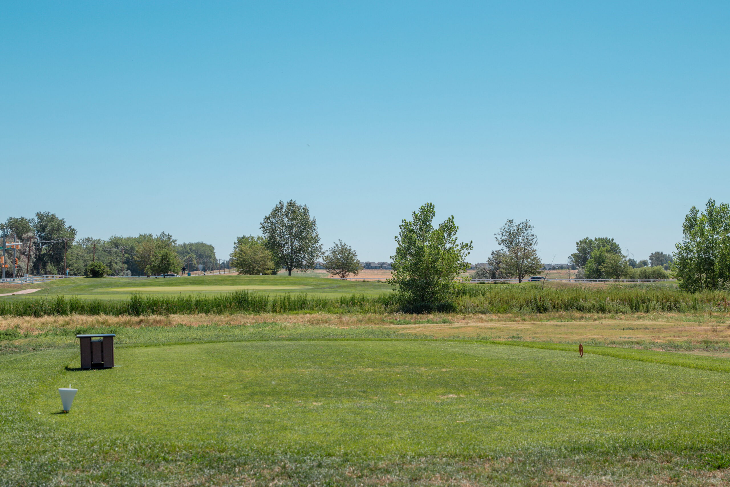 A scenic view of a golf course hole with green grass, trees, and a clear blue sky.