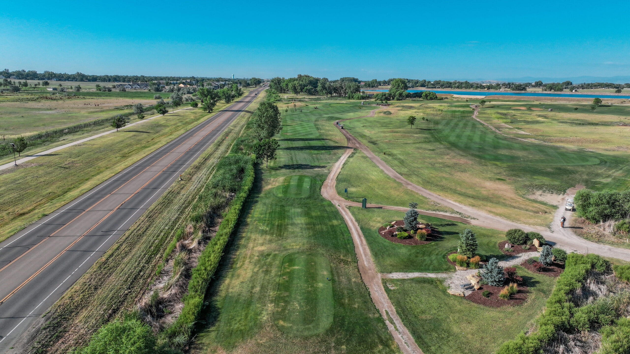 Aerial view of a golf course hole with manicured grass, a road, and landscaping features.