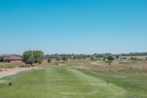 View of a golf course hole with lush green grass, trees, and a clear blue sky in the background.