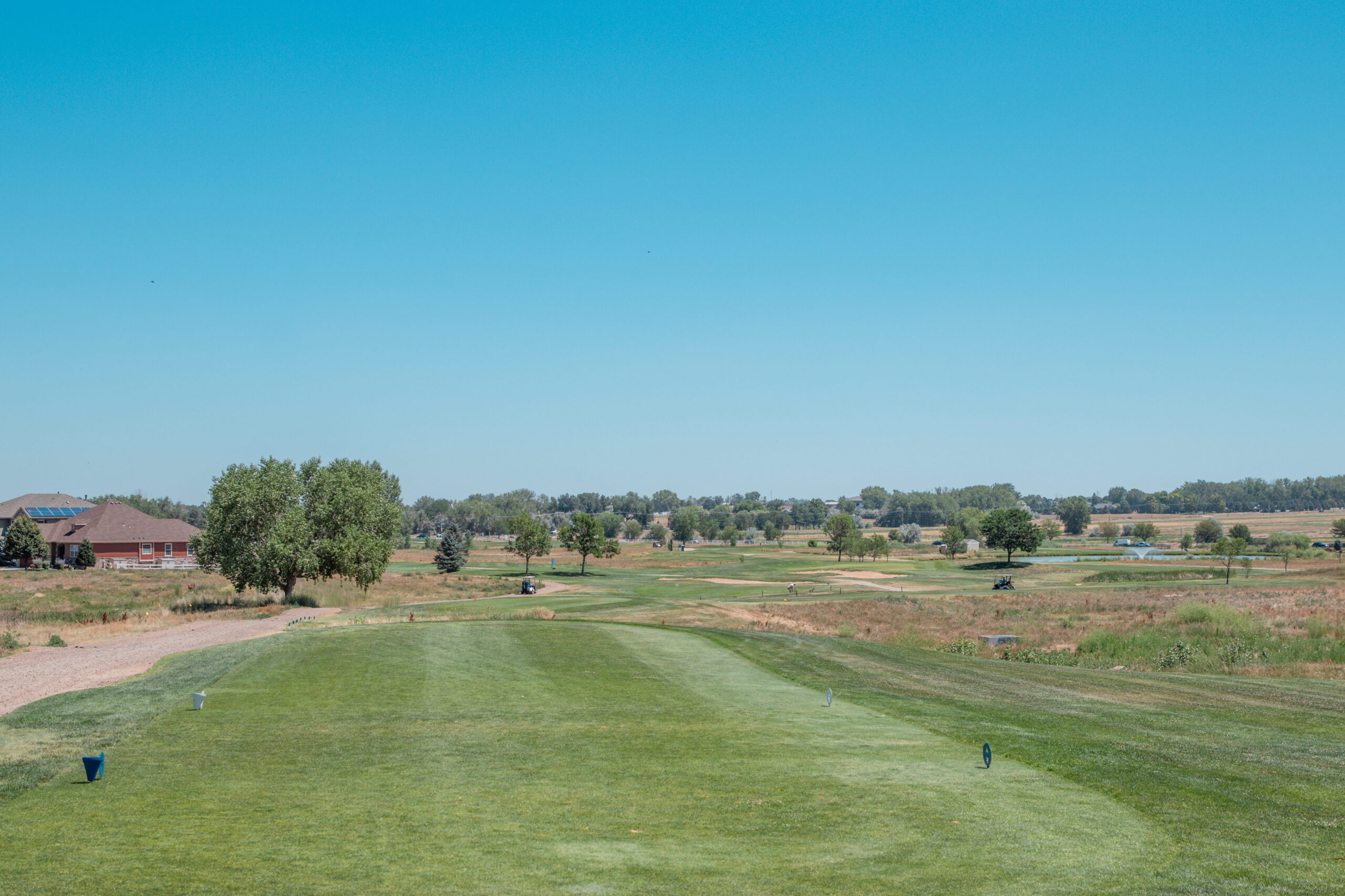 View of a golf course hole with lush green grass, trees, and a clear blue sky in the background.