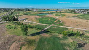 Aerial view of a golf course with green fairways, sand traps, and a pond under a clear blue sky.